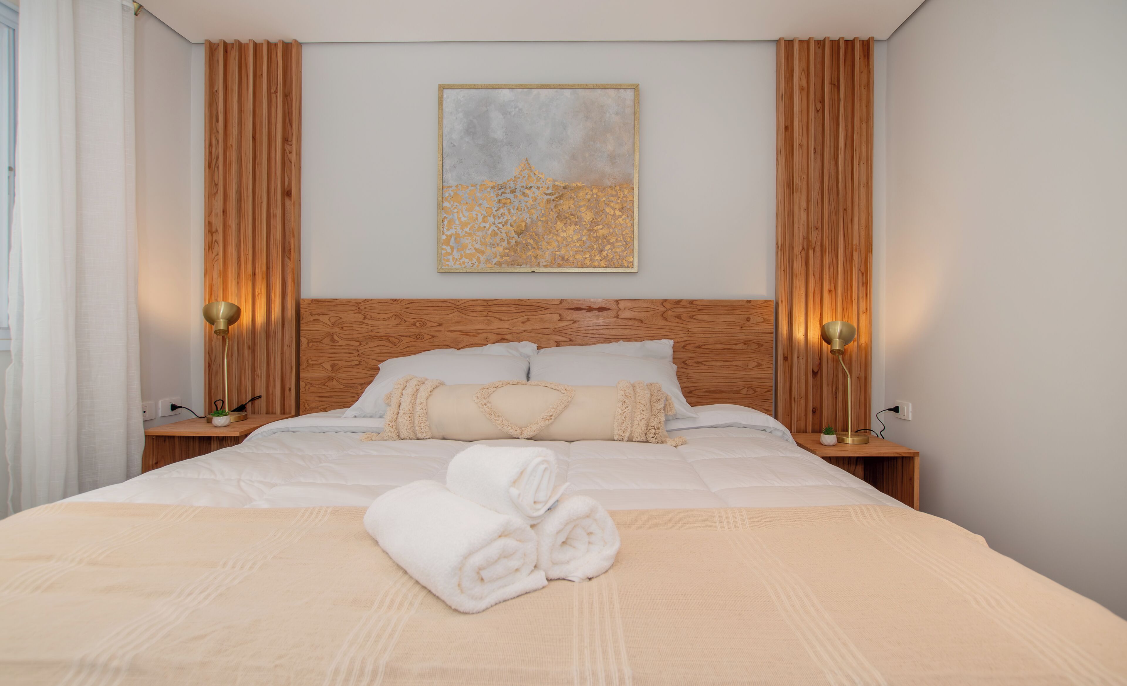 A neatly made bed with a headboard, a bedside lamp, and a small potted plant on the nightstand.