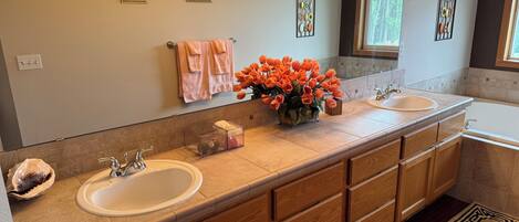 Une salle de bain moderne avec deux vasques, des meubles en bois, un grand miroir et un vase décoratif rempli de fleurs oranges.