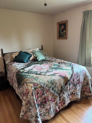 Een slaapkamer met een bloemenbedekking, een houten hoofdbord, een nachtkastje en een schilderij aan de muur.