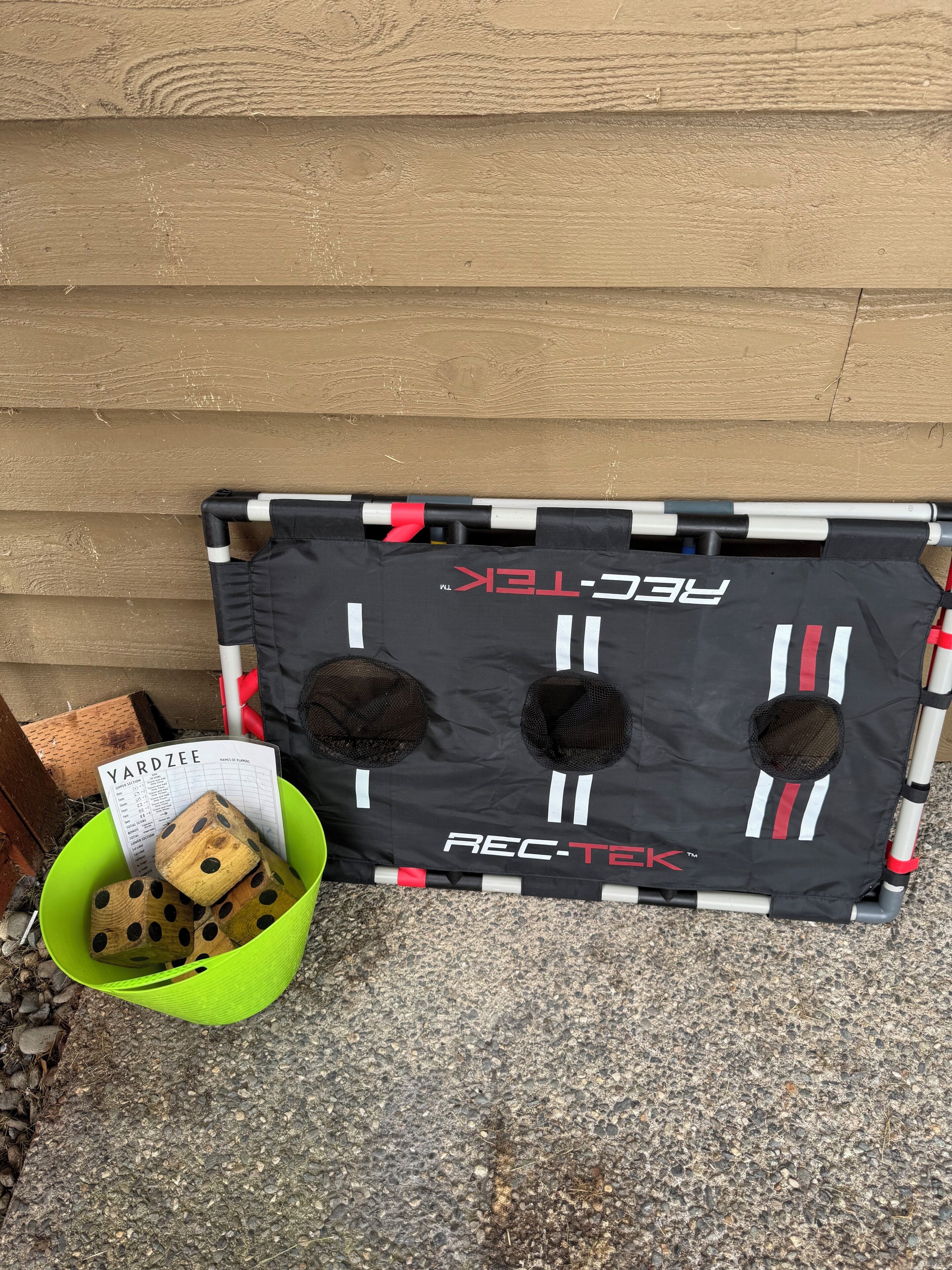 A black REC-TECK branded item with mesh pockets, a green bucket with wooden dice, and a 'YARDZEE' nameplate.