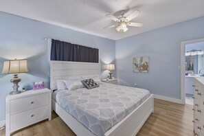 A bedroom with a bed, nightstands, a ceiling fan, a window with curtains, and a bathroom visible through an open door. - Waterfront Fun & Mini Golf, Heated Salt Water Pool & Game Room (Port Charlotte)