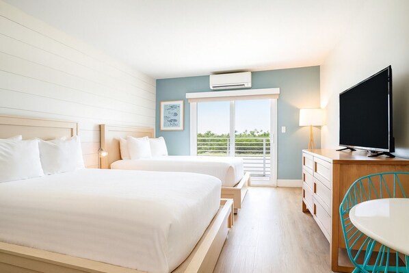 Ein Hotelzimmer mit zwei Betten, einem Fernseher, einem Schreibtisch und einem Balkon mit Blick.