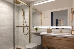 Ein modernes Badezimmer mit einer Duschkabine aus Glas, einer weißen Toilette und einem Waschtisch mit Spiegel.