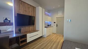 A modern kitchen with a built-in TV, wooden cabinets, and a small dining area.