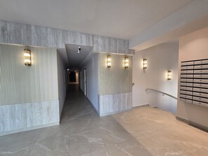 Un pasillo moderno de hotel con piso de mármol, paneles de madera clara y luminarias fijadas a la pared.