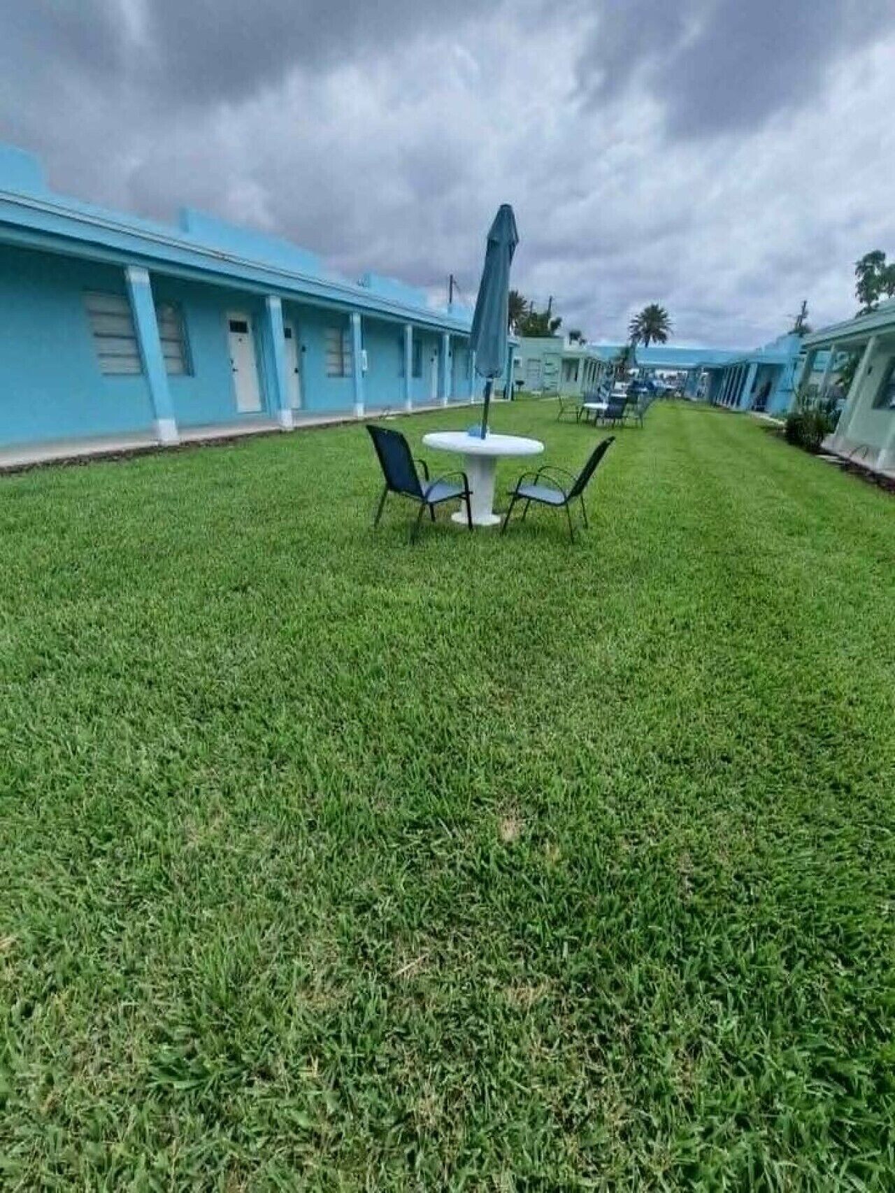 A grassy outdoor area with a round table and two chairs, surrounded by blue buildings with a consistent architectural style.