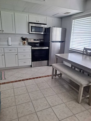 Una cocina con gabinetes blancos, microondas, refrigerador, estufa y un banco.