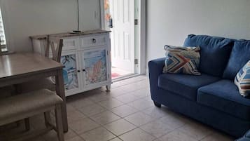 A living room with a blue sofa, a wooden table, and a television mounted on the wall.