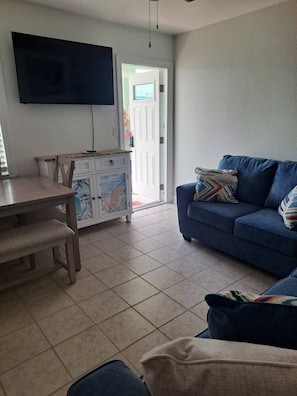 Una sala de estar con un sofá azul, una mesa de madera y un televisor montado en la pared.