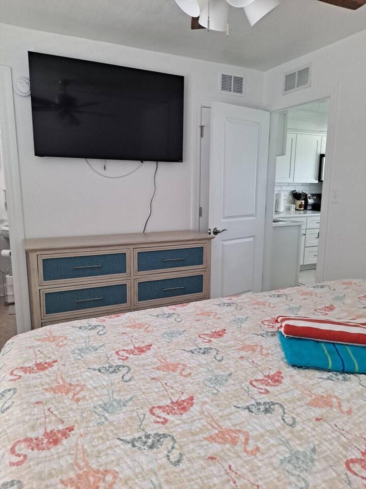 A bedroom with a bed, a dresser, a television mounted on the wall, and a door leading to a bathroom.