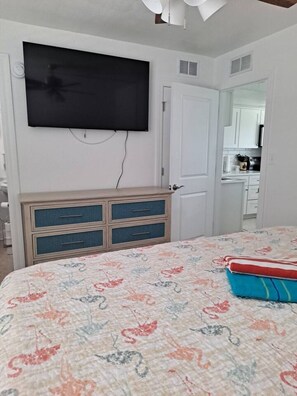 Un dormitorio con una cama, un aparador, un televisor montado en la pared y una puerta que da a un baño.