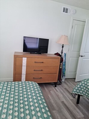 Ein Zimmer mit einem Holzkasten, einem Fernseher darauf, einer Lampe und zwei Betten mit gemusterten Bettbezügen.