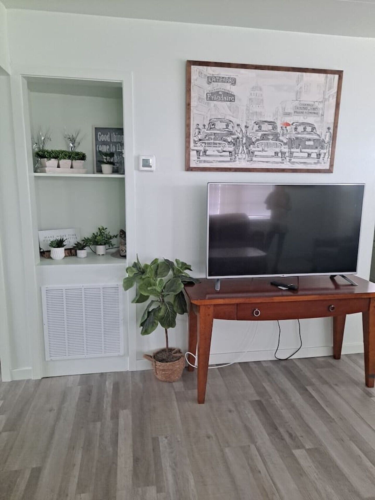 A room with a TV on a wooden stand, a potted plant, and a framed picture on the wall.