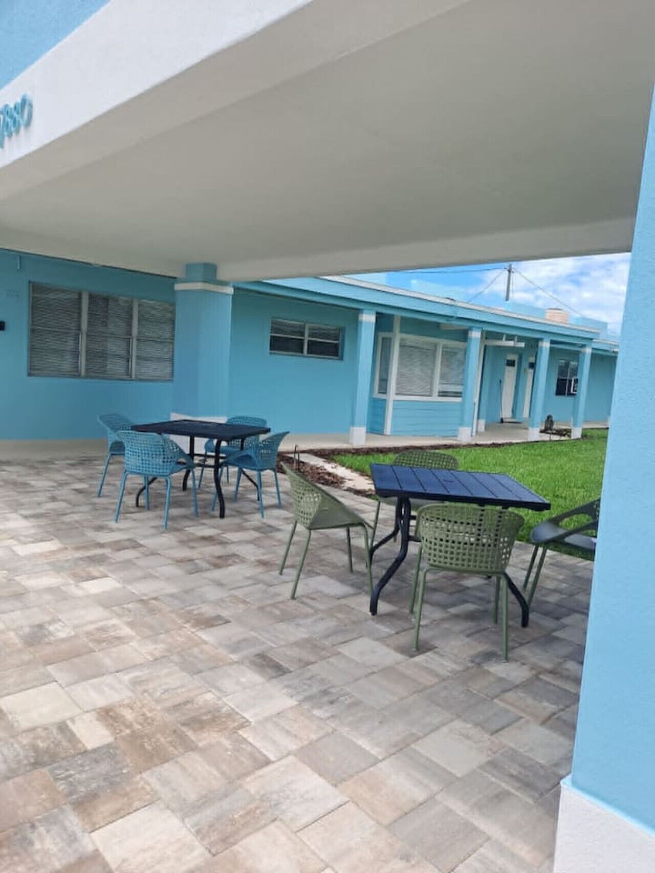 A covered patio area with outdoor seating, a tiled floor, and a building with blue walls and a white roof.