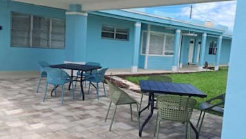 A covered patio area with outdoor seating, a tiled floor, and a building with blue walls and a white roof.