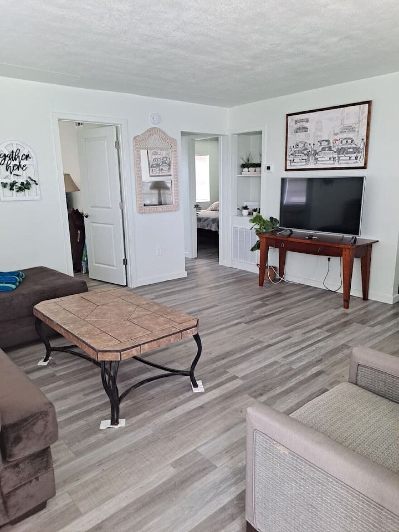 Un salon avec un canapé marron, une table basse, un téléviseur posé sur un meuble en bois et une porte donnant sur une autre pièce.
