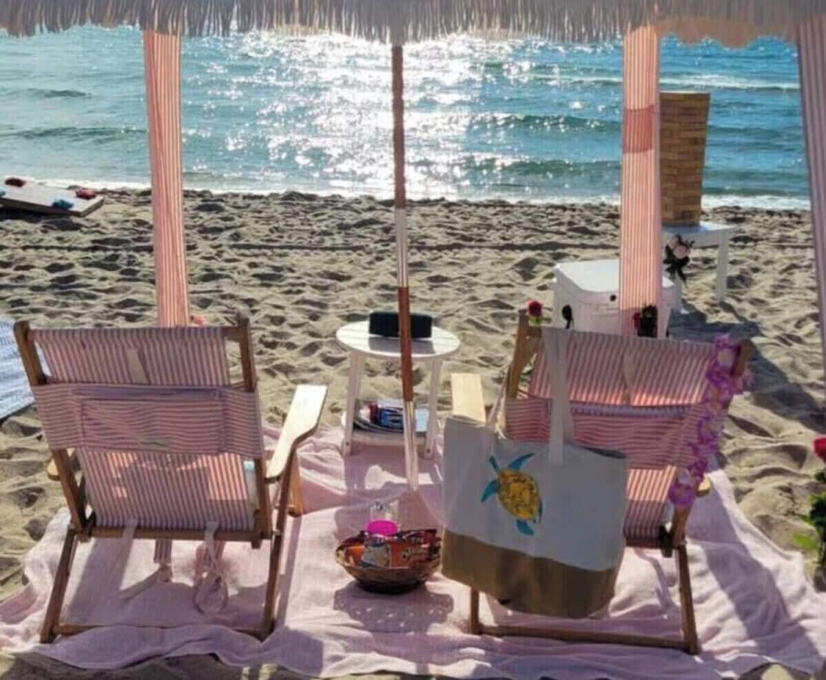 A beachside seating area with striped chairs, a table, and a sun umbrella.