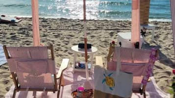 A beachside seating area with striped chairs, a table, and a sun umbrella.