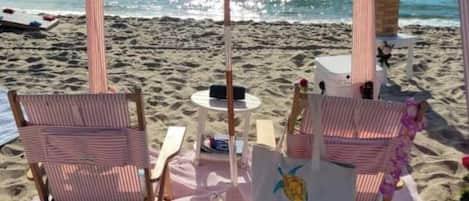 Ein Sitzbereich am Strand mit gestreiften Stühlen, einem Tisch und einem Sonnenschirm.