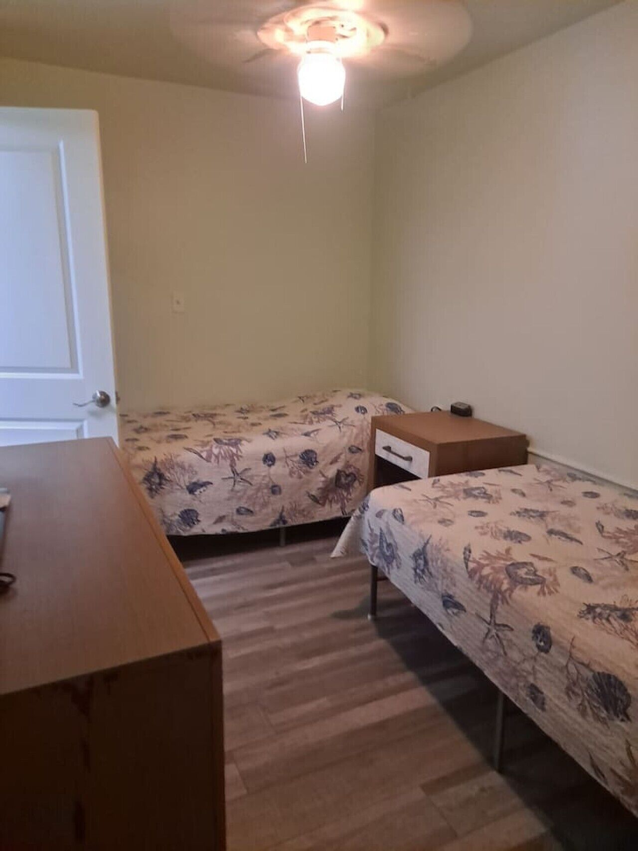 A bedroom with two single beds, a wooden dresser, and a ceiling fan.