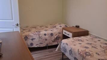 A bedroom with two single beds, a wooden dresser, and a ceiling fan.
