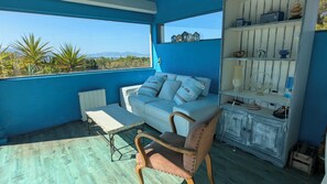 A room with a blue wall, a white sofa with pillows, a wooden chair, a small table, and a shelf with various items. - Beautiful house/villa with views of the sea and hills in Marseille (Marseille)