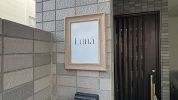 Un cartel enmarcado con el nombre 'Luna' sobre una pared texturizada, un intercomunicador de seguridad, una puerta con cerradura y un suelo de estampado de cuadros.