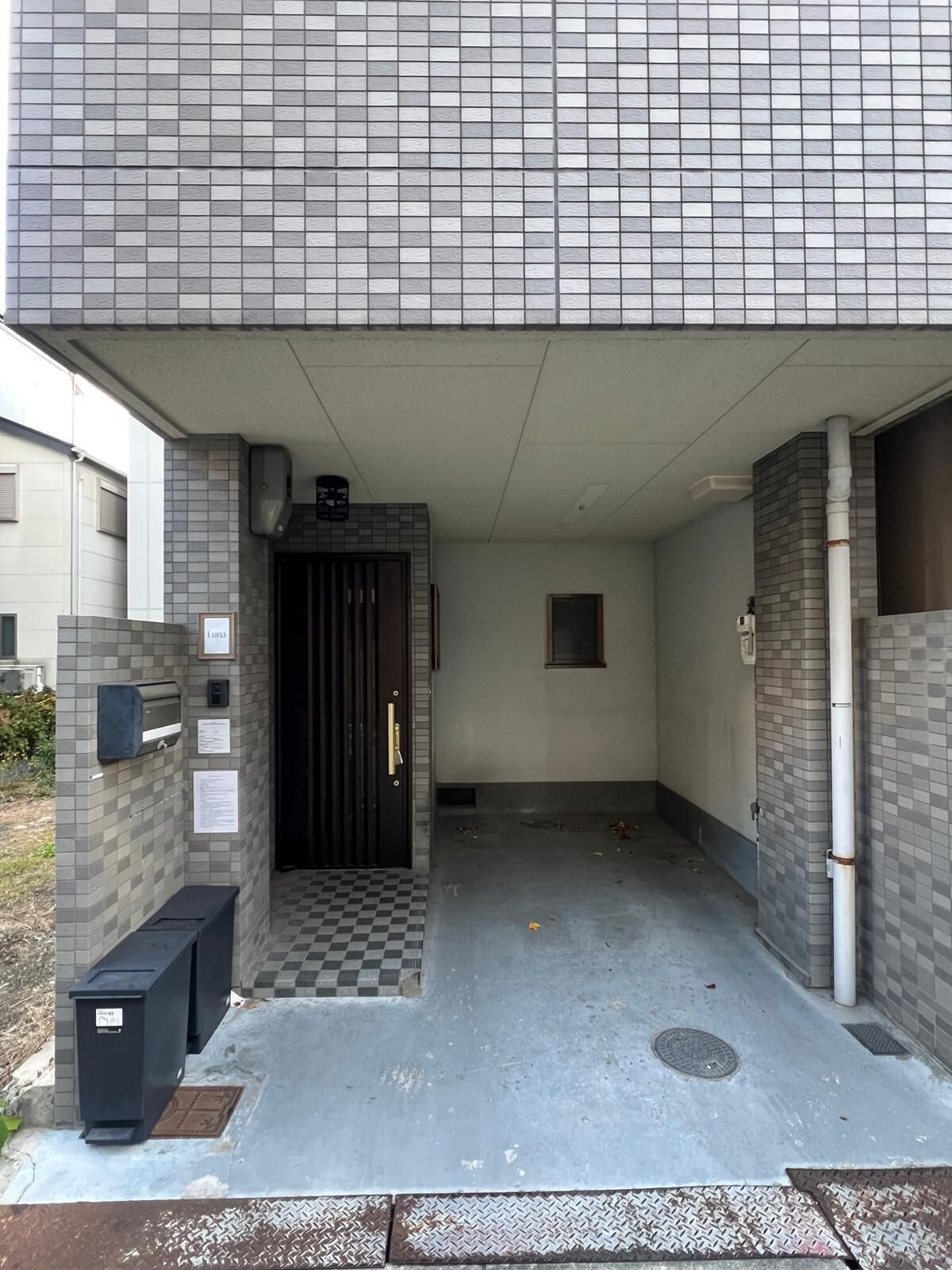 A covered entrance with a checkered floor, a door, and a trash bin.