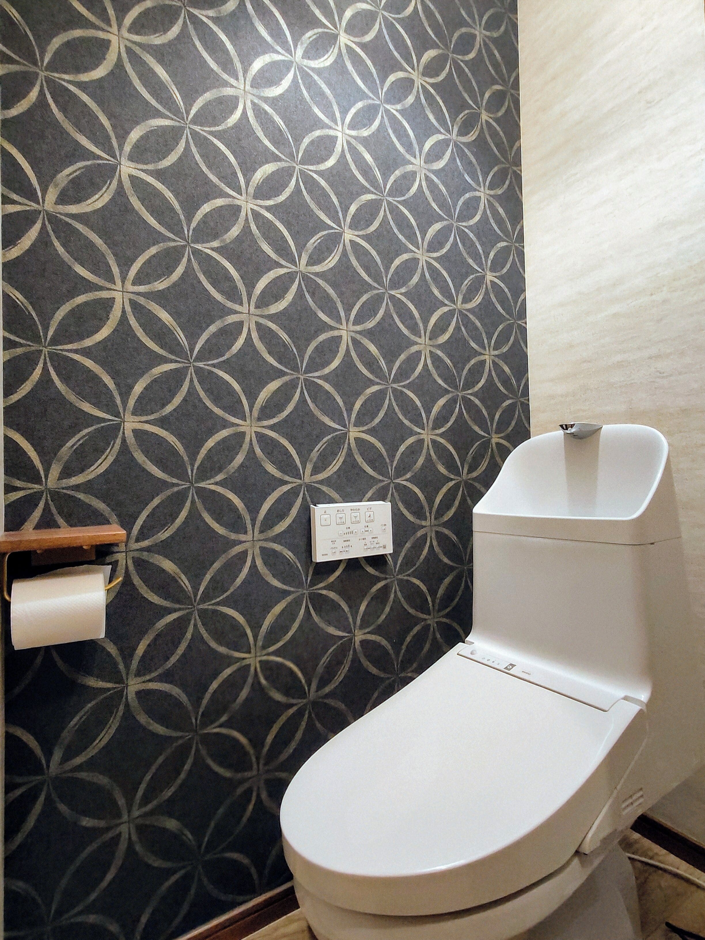 A bathroom with a patterned wall, a toilet, and a paper towel holder.