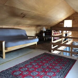 A cozy room with a wooden ceiling, a sofa, a patterned rug, and a window. - Mascoma Lake Quiet Cottage - Lakefront living! (Lebanon)