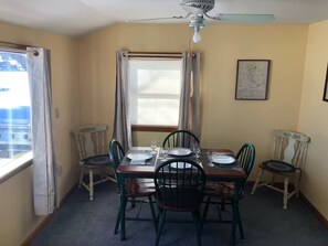A dining room with a table set for four, chairs, a ceiling fan, and a window with curtains. - Mascoma Lake Quiet Cottage - Lakefront living! (Lebanon)
