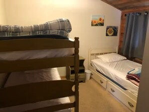 A bedroom with a bunk bed, a single bed, a bedside table, a small chair, and a wall with two sunflowers. - Mascoma Lake Quiet Cottage - Lakefront living! (Lebanon)