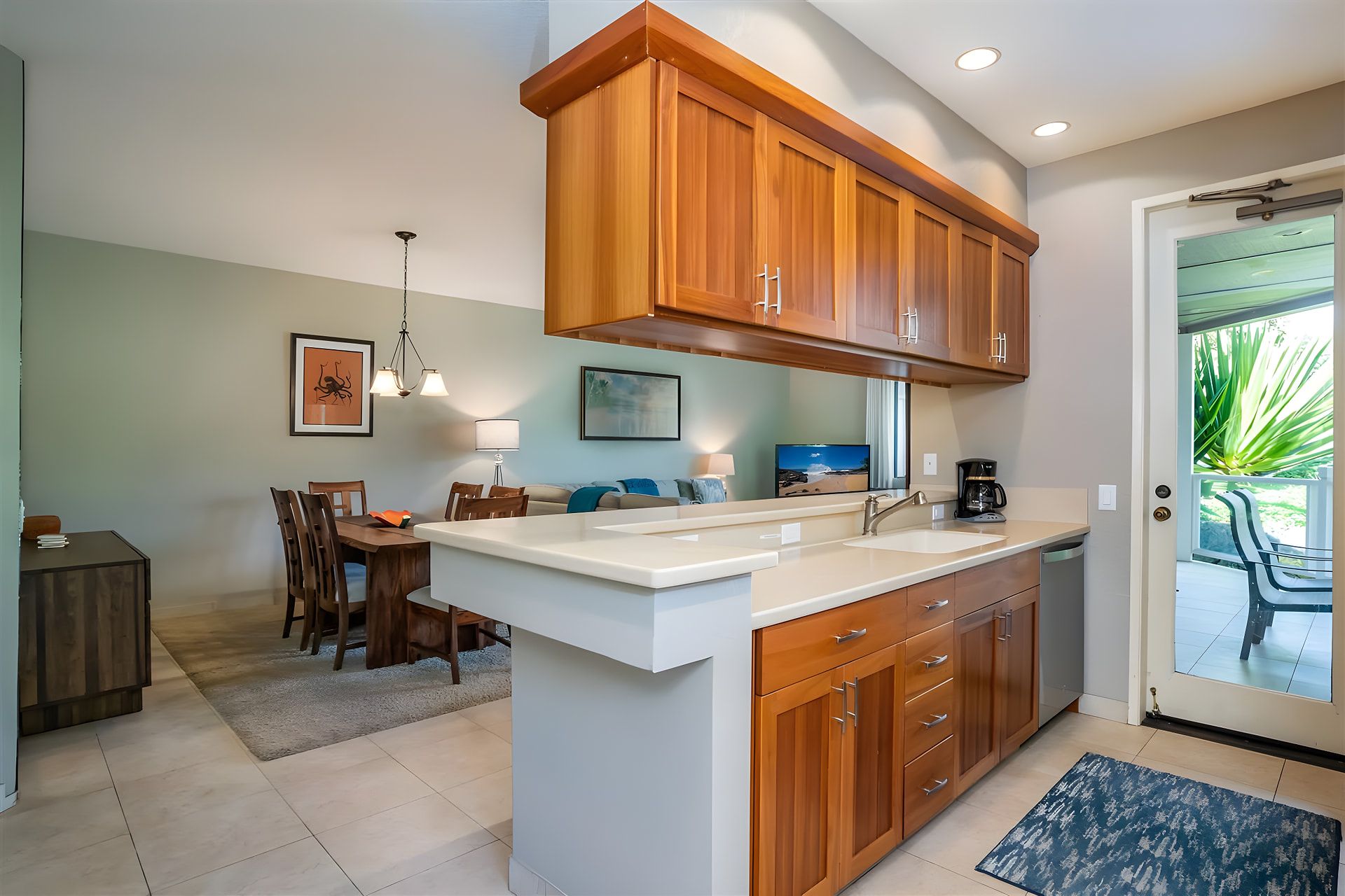 A modern kitchen with wooden cabinets, a white countertop, and a dining area with a table and chairs.