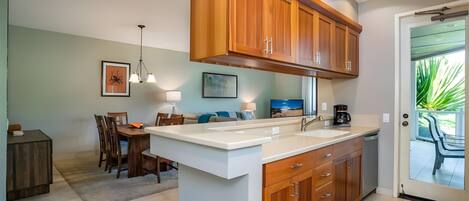 A modern kitchen with wooden cabinets, a white countertop, and a dining area with a table and chairs.