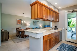 A modern kitchen with wooden cabinets, a white countertop, and a dining area with a table and chairs. - Wailea, Grand Champions Villas, Spacious 6 BR, Ocean View, Sleeps 16 (Wailea)