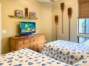 A room with a bed, a television, wooden furniture, and decorative items on the wall. - Wailea, Grand Champions Villas, Spacious 6 BR, Ocean View, Sleeps 16 (Wailea)