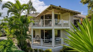Une maison à deux étages dotée d’un balcon, entourée d’une végétation luxuriante.