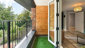 A balcony with a metal railing, a wooden wall, and a door leading to an interior space with a patterned rug and a hanging light fixture. - Woodland View 1 By My Getaways (Brighton)