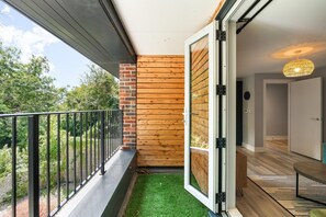 Ein Balkon mit Metallgeländer, einer Holzwand und einer Tür zu einem Innenraum mit einem gemusterten Teppich und einer hängenden Leuchte.