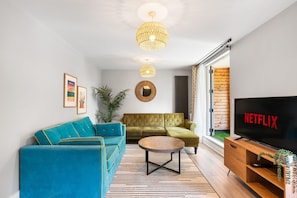 A modern living room with a blue sofa, a green sofa, a coffee table, and a TV displaying 'NETFLIX'. - Woodland View 1 By My Getaways (Brighton)