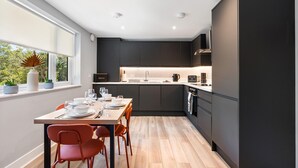 A modern kitchen with dark cabinetry, a central island, and a dining area with a table set for four. - Woodland View 1 By My Getaways (Brighton)