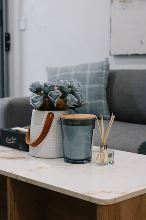 A room with a white marble table, a grey sofa, a grey pillow, a white textured bag, a blue container, and a small glass with reed sticks. - Stylish Townhouse | Double Garage | Great Location (Everton Park)