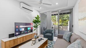 A modern living room with a flat-screen TV, a ceiling fan, a large window, and a sliding glass door leading to an outdoor area.