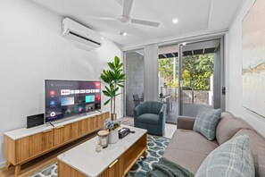 Ein modernes Wohnzimmer mit Flachbildfernseher, Deckenventilator, großem Fenster und einer Glasschiebetür, die zu einem Außenbereich führt.