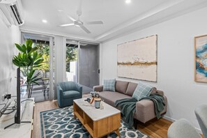 Ein modernes Wohnzimmer mit einer Couch, einem blauen Sessel, einem Couchtisch und einem Deckenventilator.