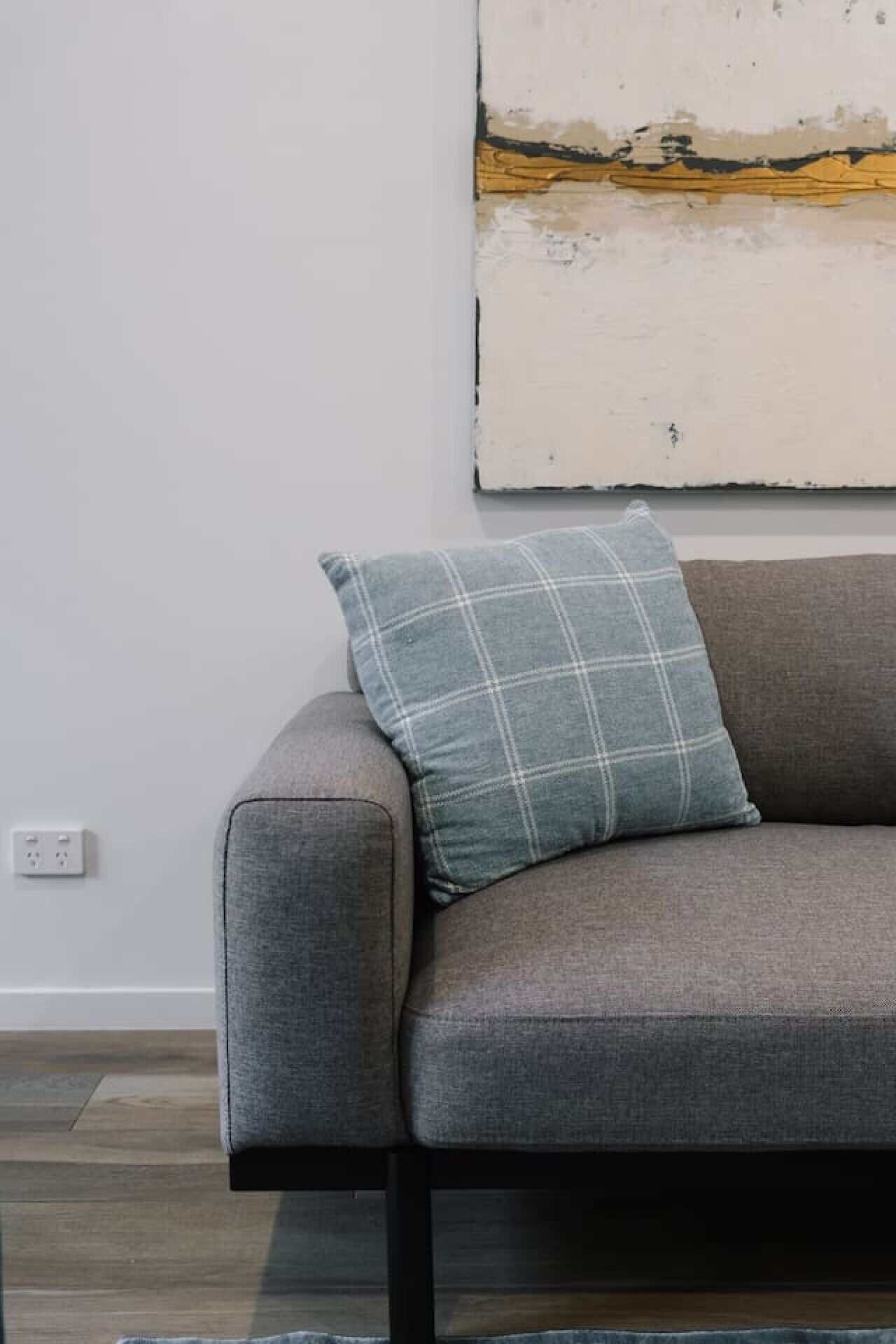 Un canapé gris avec un coussin à carreaux, placé contre un mur uni près d’une prise de courant.