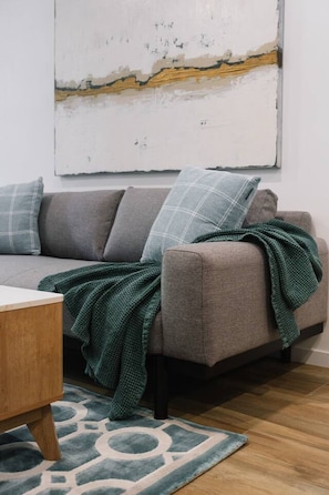 Ein Wohnzimmer mit einem grauen Sofa, einer grünen Decke und einem gemusterten Teppich.