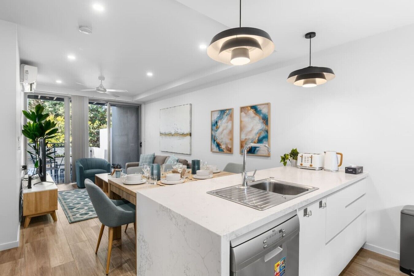 A modern kitchen with a central island, a dining area with a blue chair, and a view through a glass door.