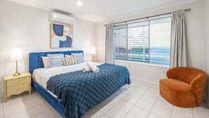 A bedroom with a bed, a nightstand, a chair, a window with curtains, and an air conditioning unit. - Heart of Sunnybank | Prime Location | Great Value (Sunnybank)
