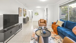 A modern living room with a flat-screen TV, a sofa, a coffee table, and a large window. - Heart of Sunnybank | Prime Location | Great Value (Sunnybank)